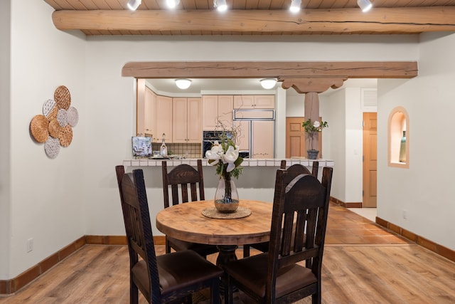 dining room featuring light wood-type flooring, wooden ceiling, beamed ceiling, and baseboards