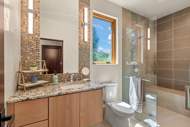 bathroom with backsplash, tile patterned floors, toilet, tiled shower, and vanity