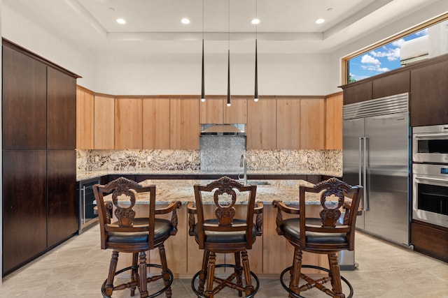 kitchen with stainless steel appliances, a kitchen breakfast bar, light stone countertops, and a kitchen island with sink