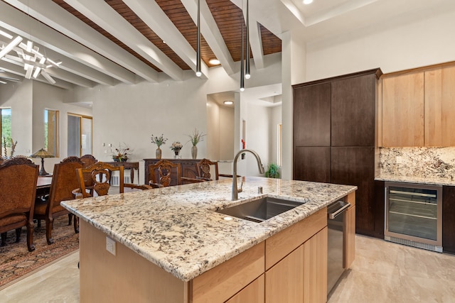 kitchen featuring light stone countertops, beamed ceiling, sink, an island with sink, and wine cooler