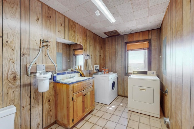 clothes washing area with sink, wooden walls, washer and clothes dryer, and light tile patterned flooring