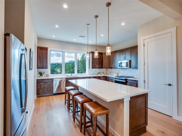 kitchen featuring appliances with stainless steel finishes, tasteful backsplash, light hardwood / wood-style floors, a kitchen island, and a breakfast bar area