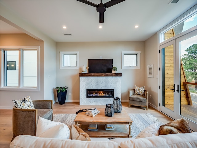 living room featuring plenty of natural light, a tiled fireplace, and light hardwood / wood-style flooring