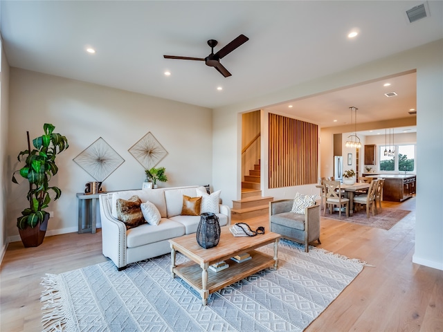 living room with ceiling fan with notable chandelier and light wood-type flooring