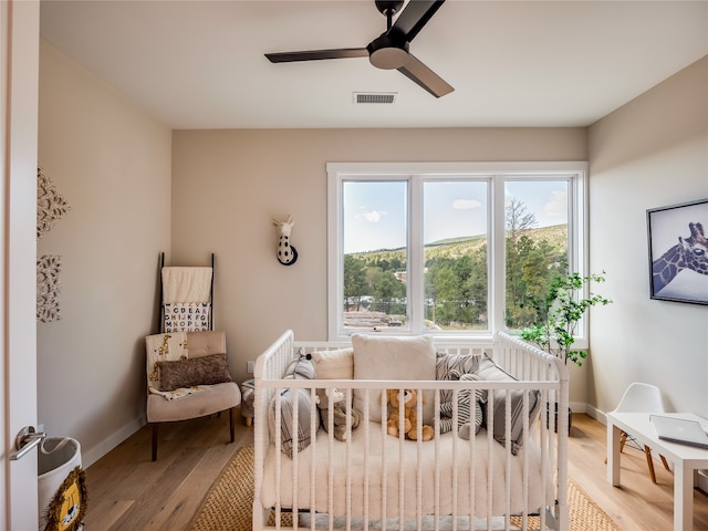 bedroom with light wood-type flooring, a nursery area, and ceiling fan