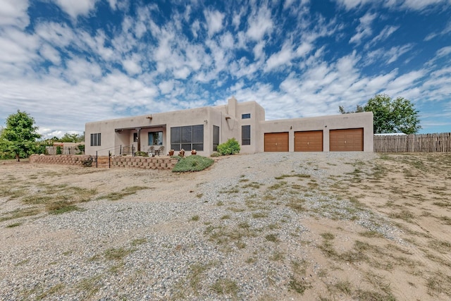 pueblo-style house featuring an attached garage, fence, and stucco siding