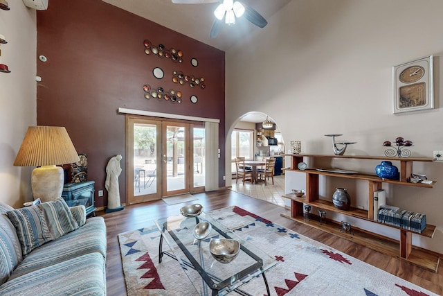 living room with arched walkways, ceiling fan, a high ceiling, wood finished floors, and french doors