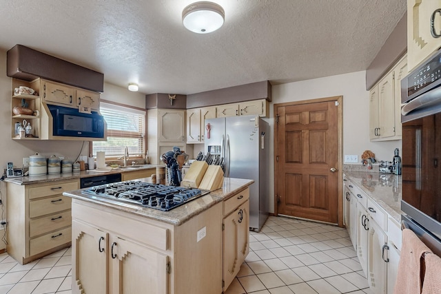 kitchen with black microwave, a kitchen island, a sink, gas stovetop, and stainless steel fridge