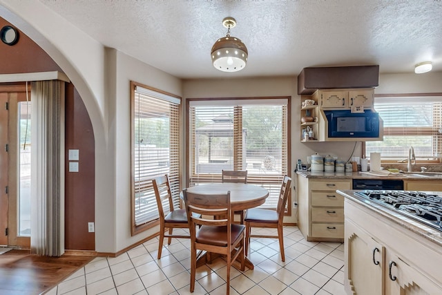 kitchen with light tile patterned floors, arched walkways, light countertops, black microwave, and a sink