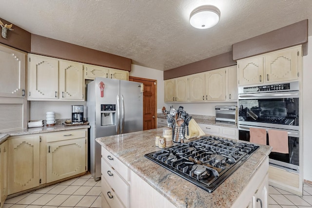 kitchen featuring light tile patterned floors, a kitchen island, appliances with stainless steel finishes, light stone countertops, and a textured ceiling