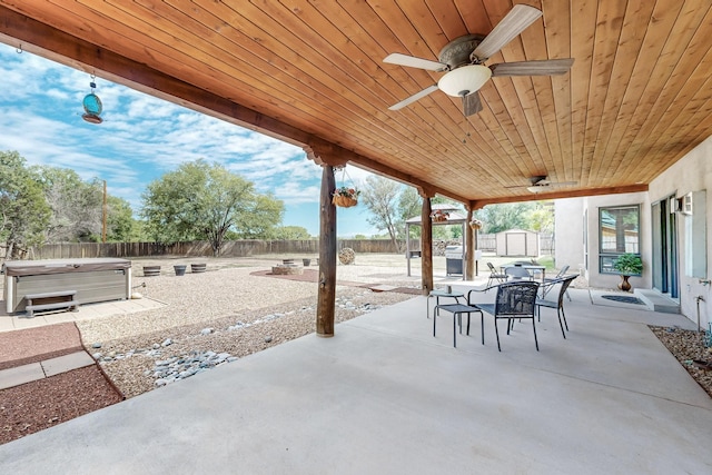 view of patio / terrace with an outbuilding, outdoor dining area, a fenced backyard, a ceiling fan, and a hot tub