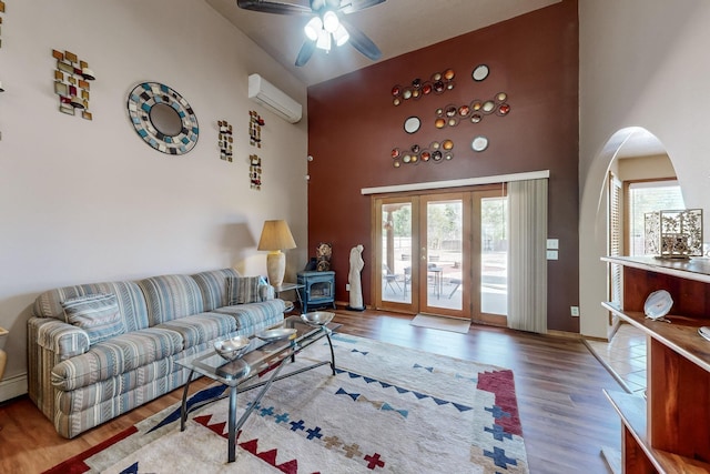 living area with ceiling fan, a high ceiling, wood finished floors, an AC wall unit, and a wood stove