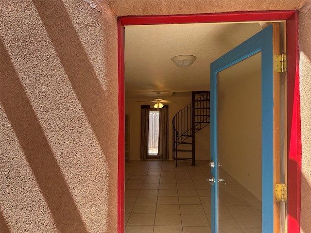 corridor featuring stairs, a textured wall, and light tile patterned floors