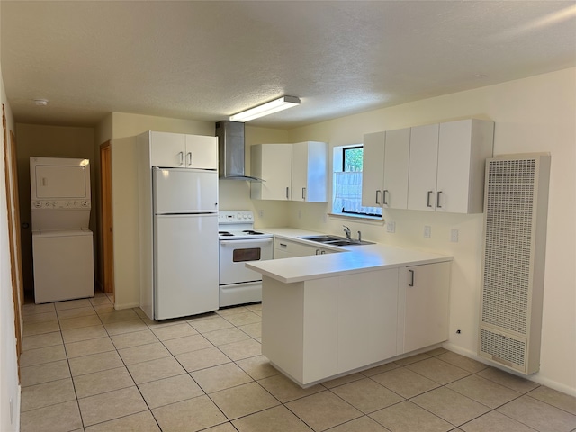 kitchen with stacked washer and clothes dryer, white appliances, wall chimney exhaust hood, sink, and white cabinets