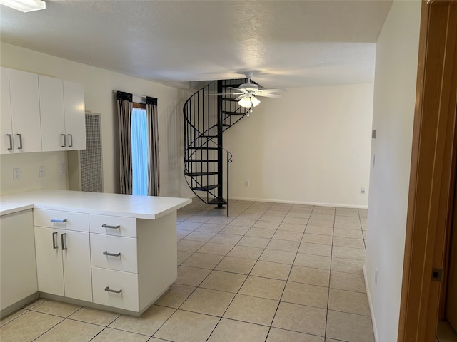 kitchen with a textured ceiling, light tile patterned floors, kitchen peninsula, ceiling fan, and white cabinets