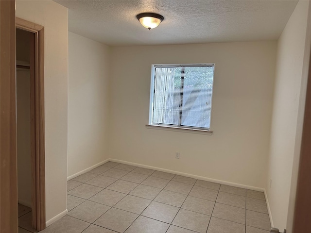 spare room featuring light tile patterned floors, baseboards, and a textured ceiling