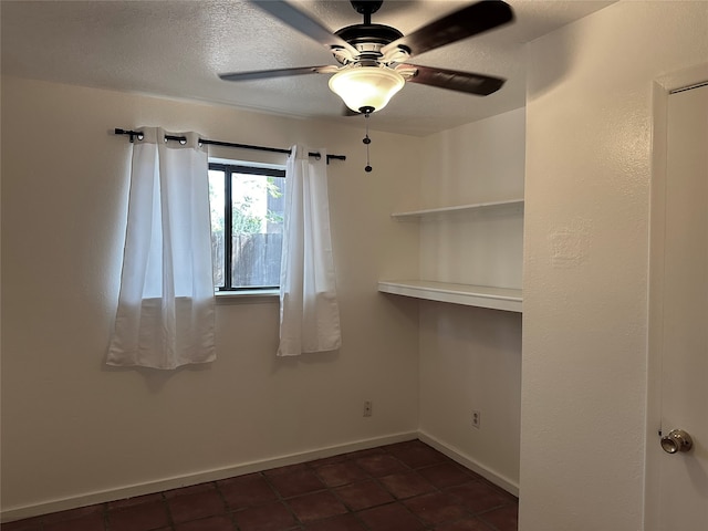 empty room with dark tile patterned flooring, a textured ceiling, and ceiling fan