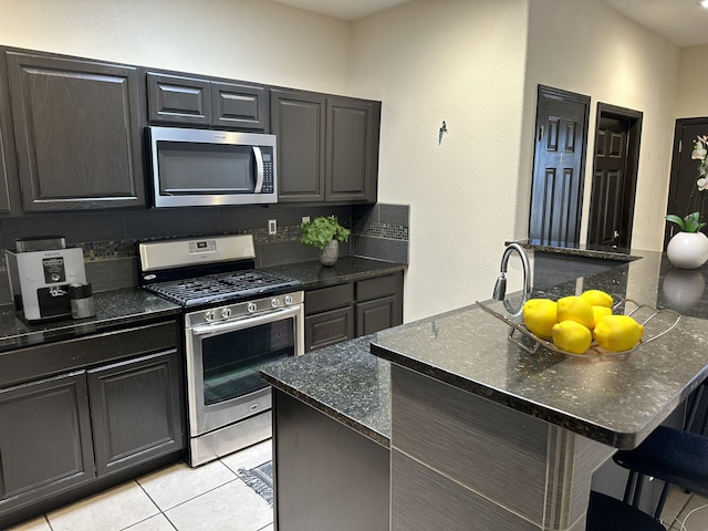 kitchen featuring light tile patterned floors, a kitchen island, stainless steel appliances, dark stone countertops, and a breakfast bar area