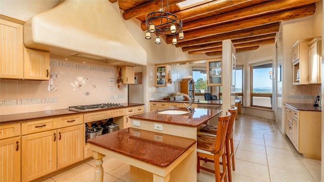 kitchen with a kitchen island with sink, light tile patterned floors, a kitchen bar, and beam ceiling