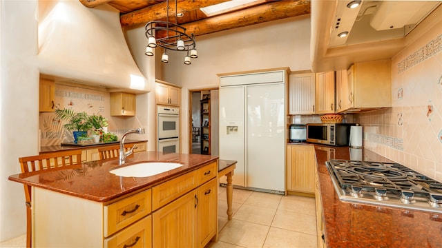 kitchen featuring a skylight, sink, stainless steel gas cooktop, paneled built in fridge, and a center island with sink