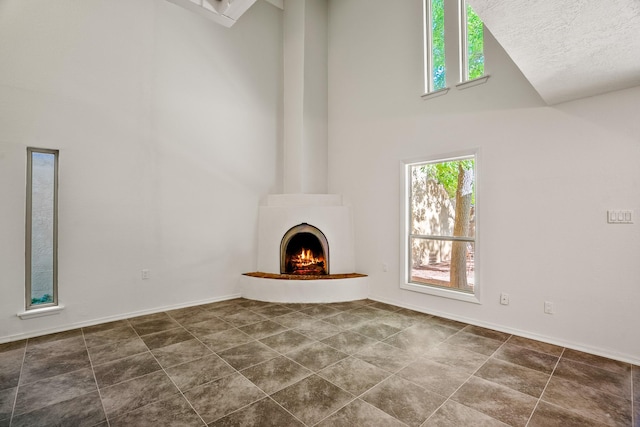 unfurnished living room featuring baseboards, high vaulted ceiling, a fireplace, and a textured ceiling