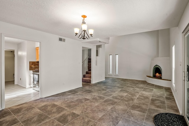 unfurnished living room with visible vents, a chandelier, stairway, a lit fireplace, and a textured ceiling