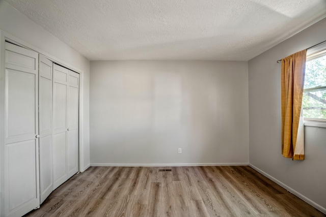 unfurnished bedroom featuring light wood-style flooring, baseboards, a closet, and a textured ceiling