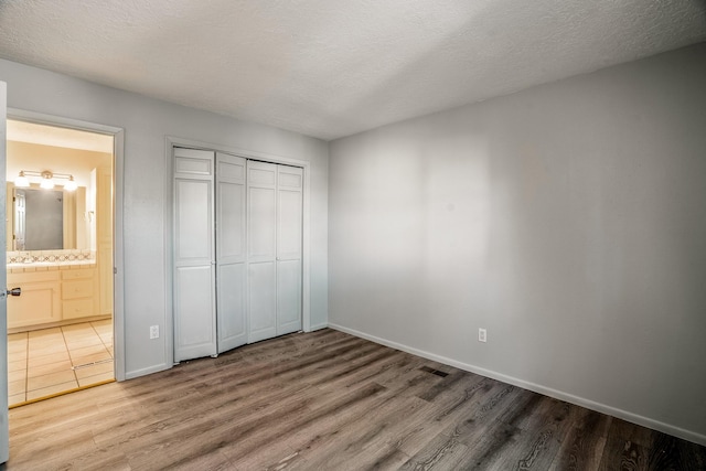 unfurnished bedroom with wood finished floors, baseboards, ensuite bath, a closet, and a textured ceiling