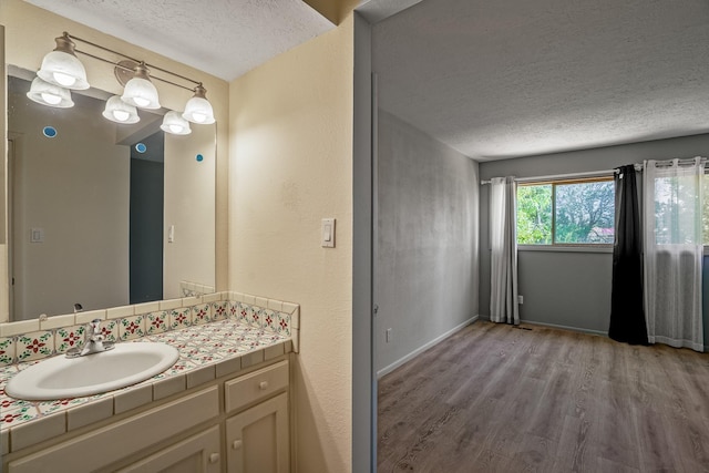 bathroom with vanity, wood finished floors, baseboards, and a textured ceiling