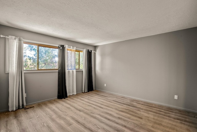 unfurnished room with light wood-type flooring, baseboards, a textured ceiling, and visible vents