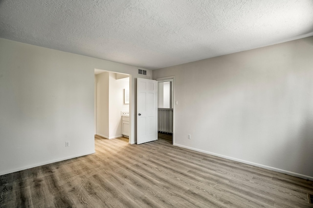 unfurnished bedroom featuring visible vents, ensuite bathroom, a textured ceiling, wood finished floors, and baseboards