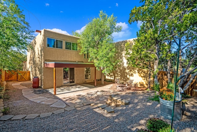 rear view of property with stucco siding, a fire pit, a patio, and fence