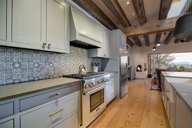 kitchen featuring light wood-type flooring, custom exhaust hood, backsplash, stainless steel appliances, and beam ceiling