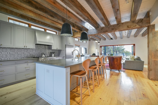 kitchen featuring a kitchen island with sink, custom range hood, beam ceiling, and light hardwood / wood-style floors