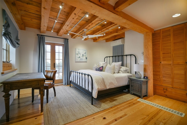 bedroom with light hardwood / wood-style flooring, an AC wall unit, rail lighting, and beam ceiling