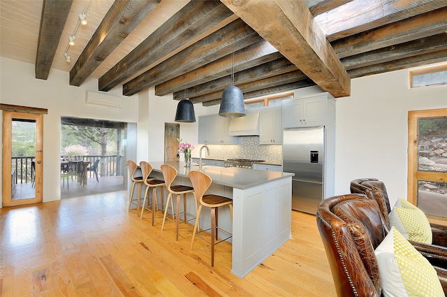 kitchen with stainless steel appliances, light hardwood / wood-style floors, beamed ceiling, rail lighting, and pendant lighting