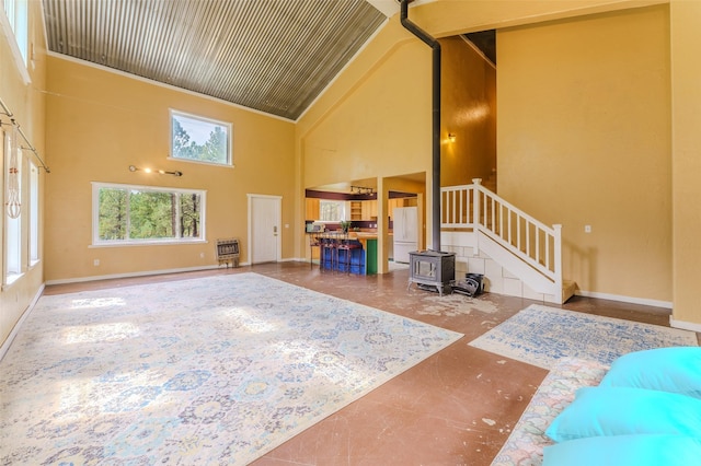 unfurnished living room with a wood stove, heating unit, and a towering ceiling