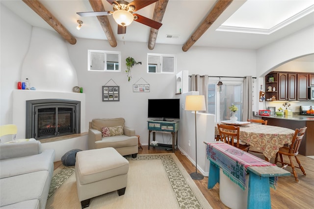 living room featuring beam ceiling, a fireplace, ceiling fan, and light hardwood / wood-style flooring