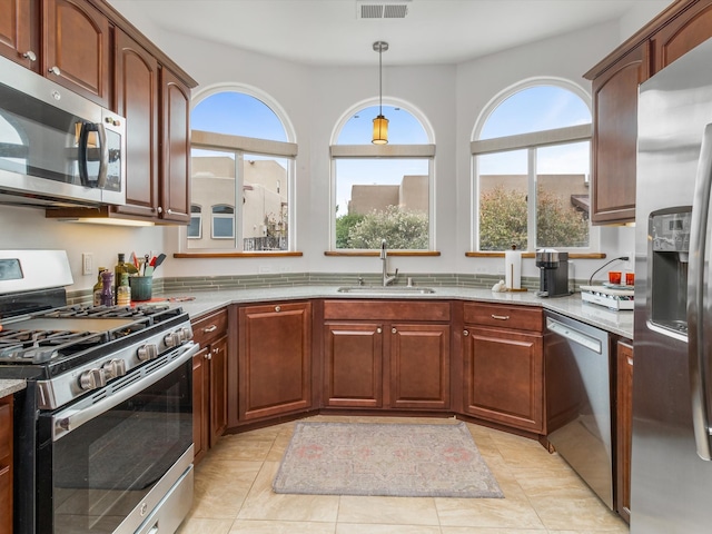 kitchen featuring sink, stainless steel appliances, light stone counters, pendant lighting, and light tile patterned floors