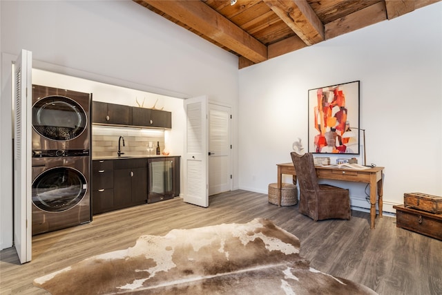 interior space featuring dark brown cabinetry, light wood-type flooring, beverage cooler, stacked washer / dryer, and beam ceiling