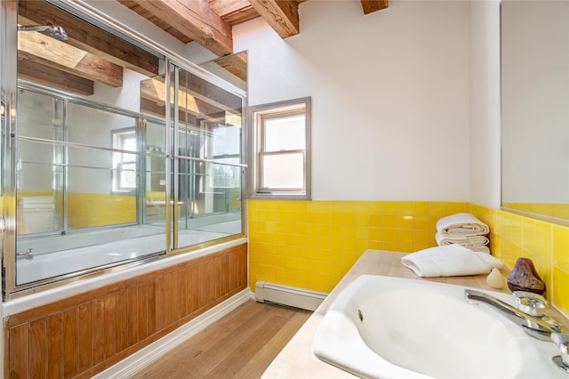 bathroom with sink, hardwood / wood-style flooring, tile walls, a baseboard heating unit, and bath / shower combo with glass door