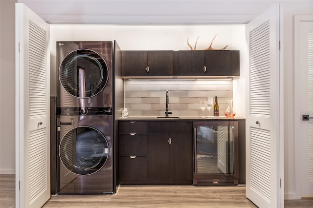 clothes washing area featuring stacked washer / drying machine, beverage cooler, indoor wet bar, and light wood-type flooring