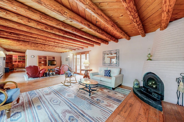 living room featuring beamed ceiling, a wood stove, light hardwood / wood-style flooring, wooden ceiling, and a fireplace