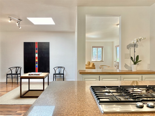 kitchen with a skylight, white cabinetry, light hardwood / wood-style floors, track lighting, and stainless steel gas stovetop