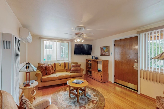 living room featuring an AC wall unit, light wood-type flooring, ceiling fan, and plenty of natural light