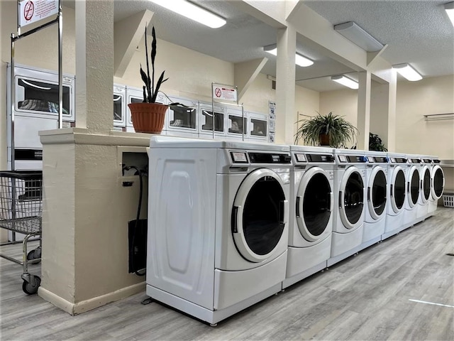 laundry room with light wood-type flooring, washer and clothes dryer, and a textured ceiling