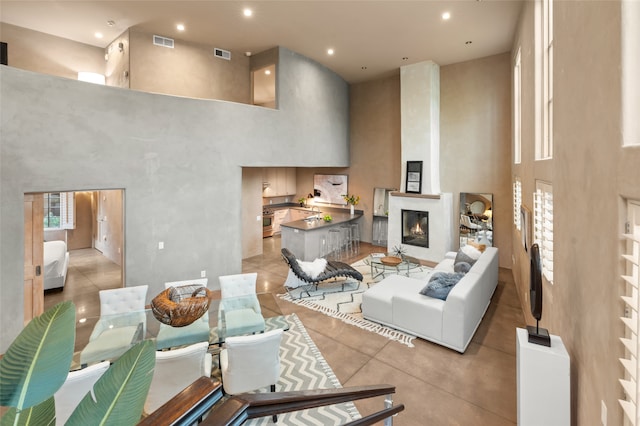 living room featuring a towering ceiling, a large fireplace, and light tile patterned flooring