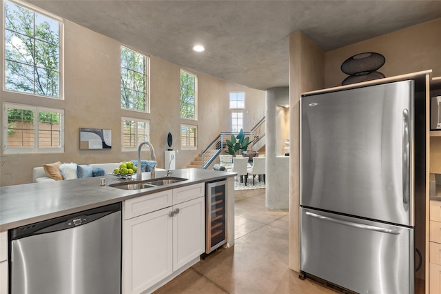 kitchen with a wealth of natural light, sink, white cabinets, beverage cooler, and stainless steel appliances