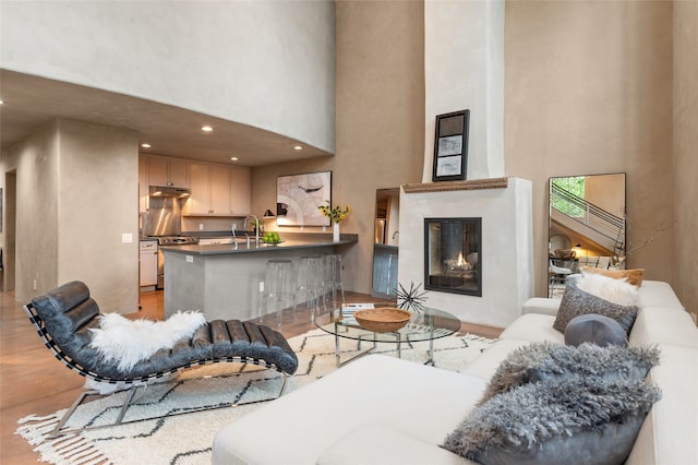 living room with sink, a fireplace, a high ceiling, and light hardwood / wood-style flooring