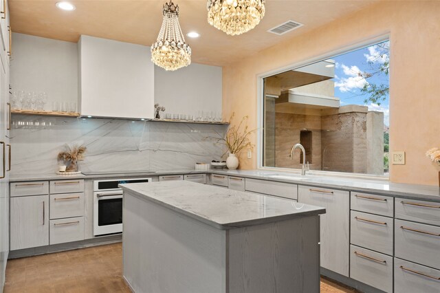 kitchen featuring backsplash, pendant lighting, a center island, sink, and a notable chandelier